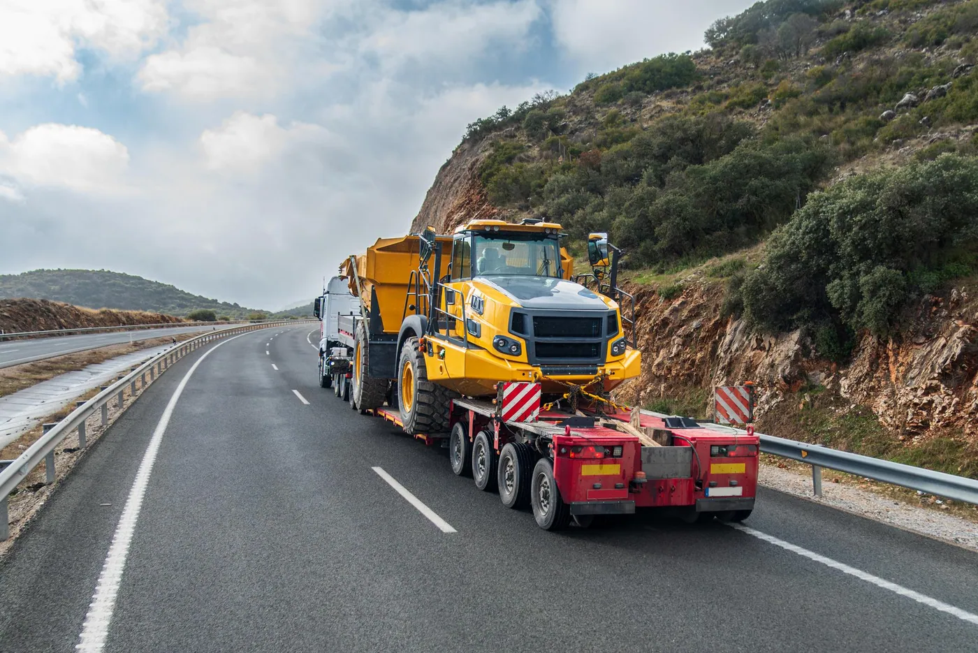 Lowbed dorse üzerinde sabitlenmiş sarı iş makinesinin karayolunda taşınması